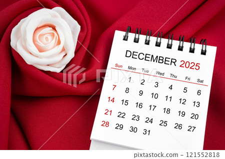 December 2025 desk calendar and pink rose on red textile. 121552818