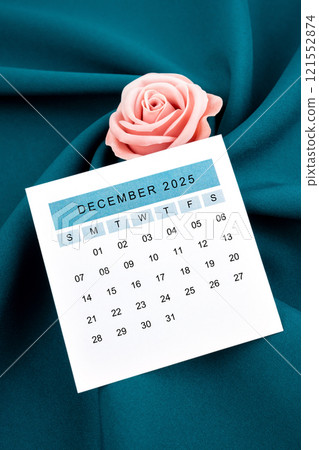 December 2025 calendar page and pink rose on green textile. December 2025 calendar page and pink rose on green textile. 121552874