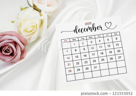 Decemeber 2025 calendar page and rose flower on white satin textile. Decemeber 2025 calendar page and rose flower on white satin textile. 121553052