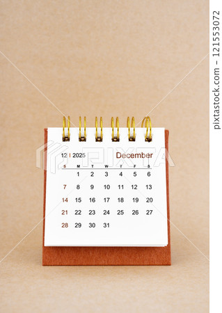 December 2025 white desk calendar on brown background. 121553072