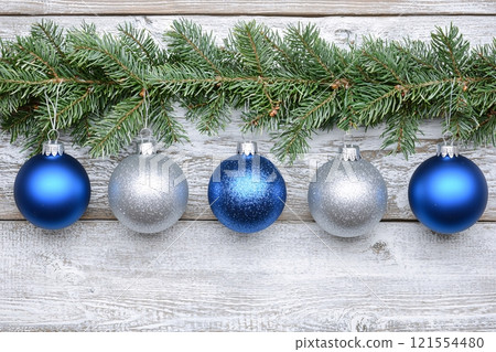 With a winter wonderland theme, elegant silver and blue Christmas ornaments dangle from frosted tree 121554480