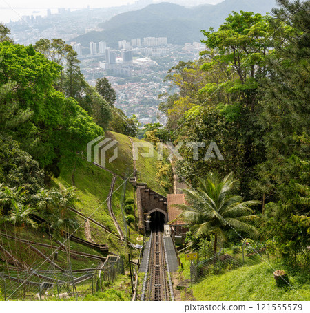 Funicular railway track on Penang Hill, Malaysia, descending through dense tropical forest, leading into tunnel, surrounded by lush greenery and palm trees, scenic view, transportation, travel 121555579