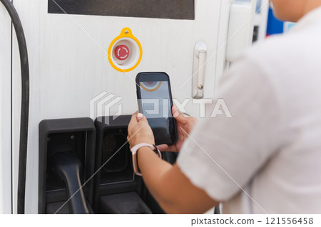 Woman going to charge electric car on vehicle public power station, scanning QR code with cell phone for paying. Woman going to charge electric car on vehicle public power station, scanning QR code with cell phone for paying. 121556458