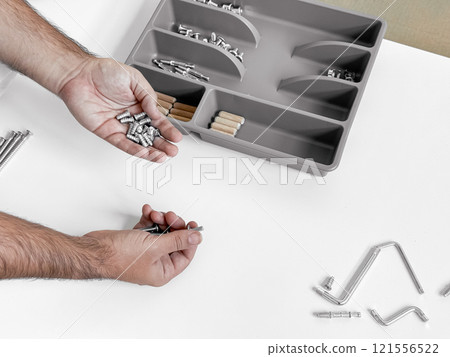 Assembling furniture. Hands organizing screws and dowels near tray 121556522