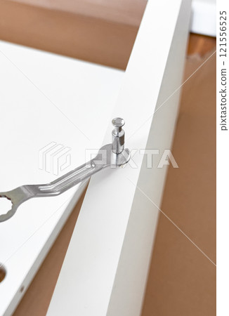 Assembling white furniture with metal wrench and cam lock fastener on brown surface 121556525