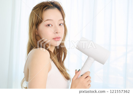 婦女用吹風機烘乾她的頭髮。 121557362