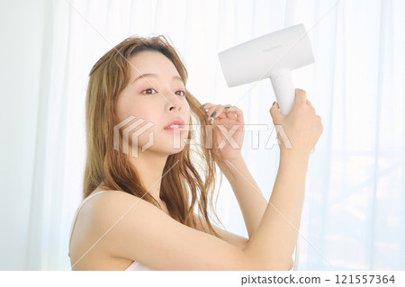 婦女用吹風機烘乾她的頭髮。 121557364