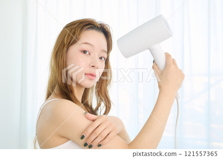 A woman drying her hair with a dryer. 121557365