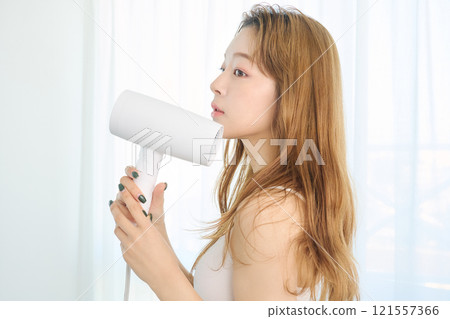 A woman drying her hair with a dryer. A woman drying her hair with a dryer. 121557366
