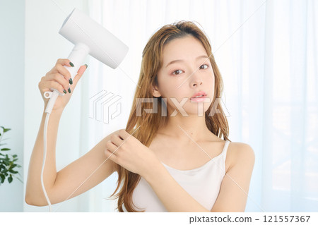 婦女用吹風機烘乾她的頭髮。 121557367