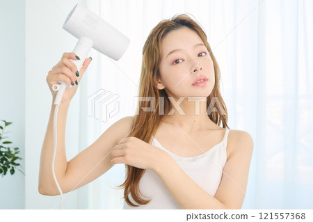 A woman drying her hair with a dryer. 121557368