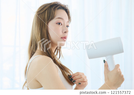A woman drying her hair with a dryer. 121557372