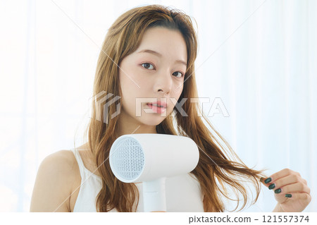 婦女用吹風機烘乾她的頭髮。 121557374