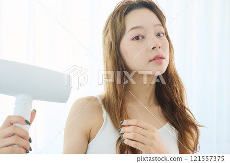 A woman drying her hair with a dryer. 121557375