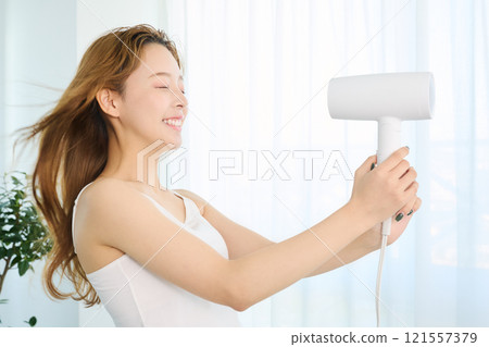 A woman drying her hair with a dryer. 121557379