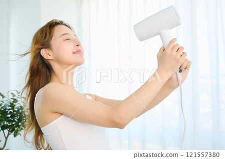 婦女用吹風機烘乾她的頭髮。 121557380