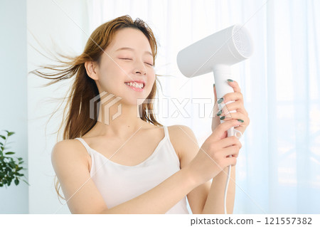 婦女用吹風機烘乾她的頭髮。 婦女用吹風機烘乾她的頭髮。 121557382