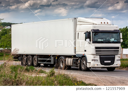 All white long-distance truck with a semitrailer moves in the countryside 121557909