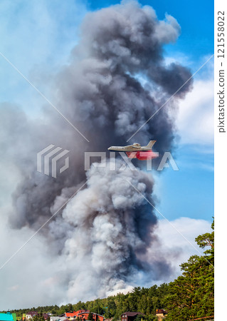 Big amphibious fire aircraft drops water on large forest fire near the village 121558022