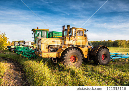 Wheeled tractors and combine harvester standing in a row on an agricultural field Wheeled tractors and combine harvester standing in a row on an agricultural field 121558116