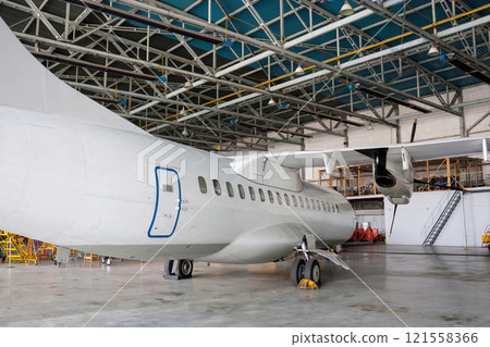 White passenger turboprop aircraft under maintenance in the hangar. Repair of airplane White passenger turboprop aircraft under maintenance in the hangar. Repair of airplane 121558366
