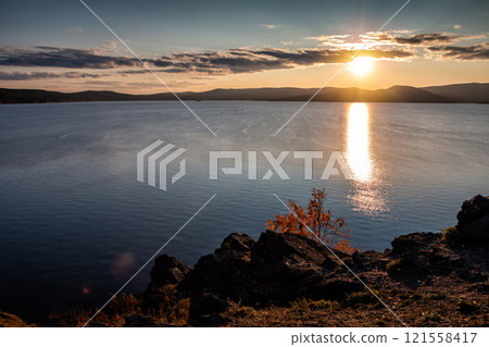 Beautiful lake and rocky shore in the rays of evening sun of golden autumn Beautiful lake and rocky shore in the rays of evening sun of golden autumn 121558417