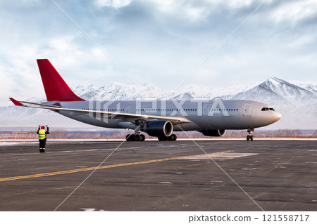 Airport marshaller meets passenger airliner on the background of high picturesque mountains 121558717