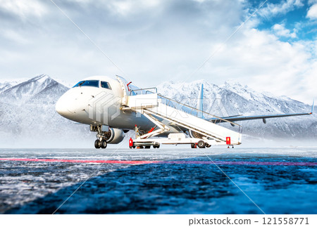 White passenger airplane with air-stairs at the airport apron on the background of high scenic mountains White passenger airplane with air-stairs at the airport apron on the background of high scenic mountains 121558771
