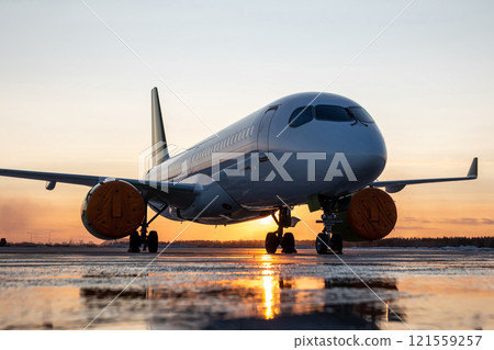 Modern passenger airplane on the airport apron against the backdrop of a picturesque sunset 121559257