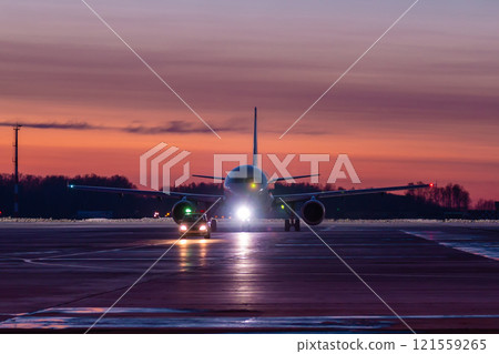 A passenger aircraft run the follow-me-car along the airport apron at a picturesque day after sunset A passenger aircraft run the follow-me-car along the airport apron at a picturesque day after sunset 121559265