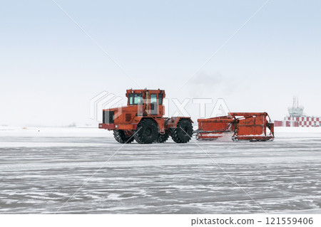 Large wheeled tractor with special equipment removes snow on the airport apron in a snowstorm Large wheeled tractor with special equipment removes snow on the airport apron in a snowstorm 121559406