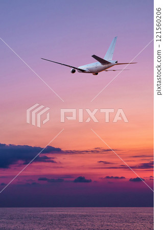 A large wide body passenger aircraft fly over the sea against the backdrop of a scenic sundown sky 121560206