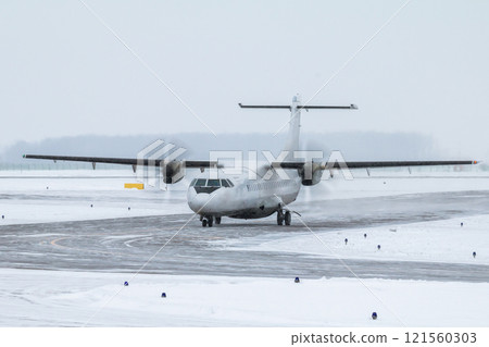 White passenger turboprop airplane taxiing on the taxiway in a severe blizzard 121560303