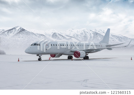 White passenger aircraft on the airport apron in a snowstorm on the background of high scenic mountains White passenger aircraft on the airport apron in a snowstorm on the background of high scenic mountains 121560315