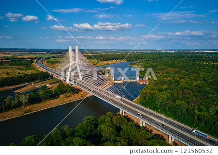 Cable stayed bridge over river surrounded by lush green forest 121560532