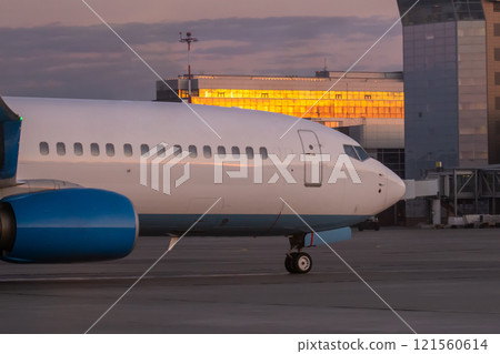 A close-up of the front of a passenger airplane. The aircraft is taxiing at the airport apron near the terminal 121560614