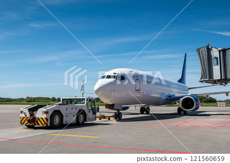 Tow tractor pushes the passenger airliner away from the jet bridge 121560659