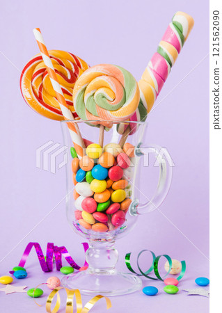 Colorful candies in cup on table on light background background. Large swirled lollipops. Creative concept of a jar full of delicious sweets from the candy store Colorful candies in cup on table on light background background. Large swirled lollipops. Creative concept of a jar full of delicious sweets from the candy store 121562090