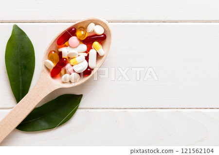 Vitamin capsules in a spoon on a colored background. Pills served as a healthy meal. Red soft gel vitamin supplement capsules on spoon 121562104