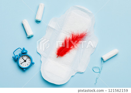 Ringing alarm clock with sanitary female tampons and menstrual sanitary pads. Medical concept of woman critical days and menstruation. Female daily hygiene. Copy space Ringing alarm clock with sanitary female tampons and menstrual sanitary pads. Medical concept of woman critical days and menstruation. Female daily hygiene. Copy space 121562159