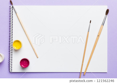 Album pages and paints, pencils, brush on a colored background. Top view with empty space. workplace for creativity. home teaching concept drawing 121562246