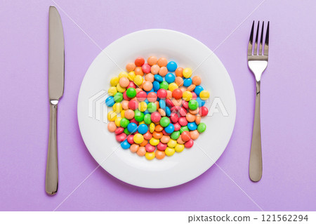 cutlery on table and sweet plate of candy. Health and obesity concept, top view on colored background cutlery on table and sweet plate of candy. Health and obesity concept, top view on colored background 121562294