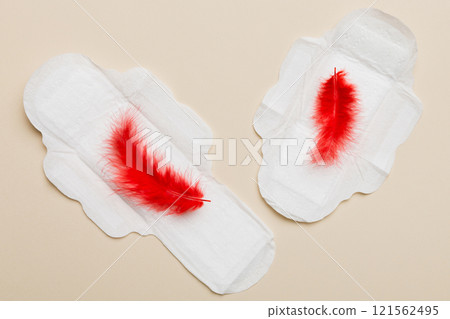 Women hygiene products or Sanitary pad with red feather on colored background. Pastel color. Closeup. Empty place for text. Female daily hygiene Women hygiene products or Sanitary pad with red feather on colored background. Pastel color. Closeup. Empty place for text. Female daily hygiene 121562495