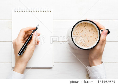 Woman hand with pencil writing on notebook and hold coffee cup. Woman working on office table with coffee 121562675