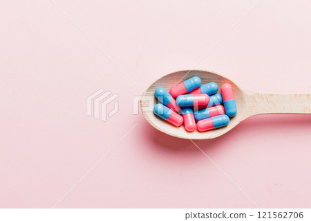 Vitamin capsules in a spoon on a colored background. Pills served as a healthy meal. Red soft gel vitamin supplement capsules on spoon 121562706