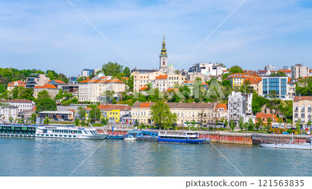 The Sava River flows through Belgrade, showcasing vibrant waterfront buildings and boats docked along the shore under a clear blue sky on a sunny day. 121563835