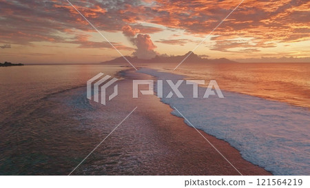 Ocean waves gently rolling sand shore of Tahiti tropical island at sunset. Vibrant orange colors and dramatic clouds reflecting in water. Remote wild nature paradise, exotic summer travel. Aerial shot Ocean waves gently rolling sand shore of Tahiti tropical island at sunset. Vibrant orange colors and dramatic clouds reflecting in water. Remote wild nature paradise, exotic summer travel. Aerial shot 121564219