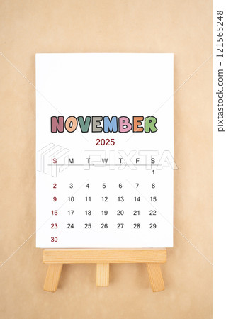 Calendar page for November 2025 with wood easel on old brown background. 121565248