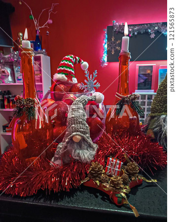 A bright red installation of a festive atmosphere. Improvised candlesticks from bottles. Christmas tree toys and a gnome in a hat. Decorative interior. 121565873
