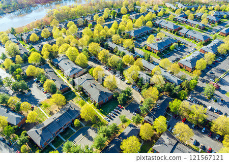 Aerial view shows cars parked in lot bordered by green trees, residential apartment buildings at American small town New Jersey 121567121